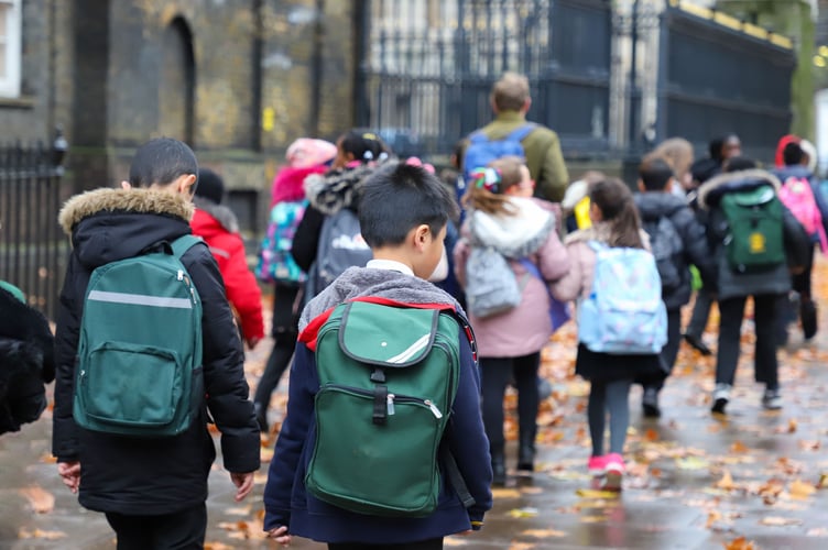 Multi-Cultural Children (asian, Indian, Chinese, Caucasian) primary student or kids and teacher carrying school bag walk in street in rain winter day, with maple leaves on ground. back view