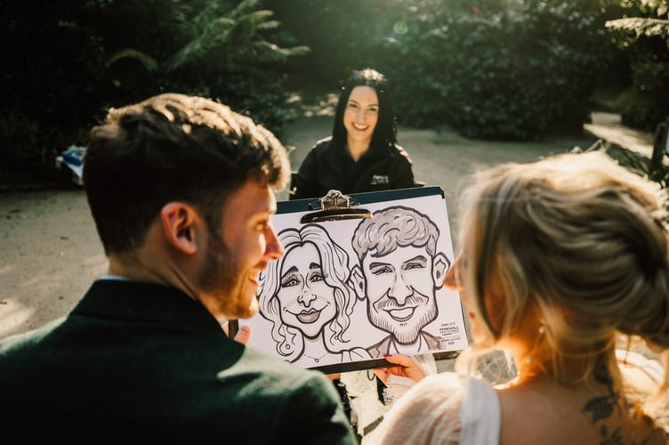 Caricaturist Cassie Kemp presents her work to a happy couple at Heligan Gardens