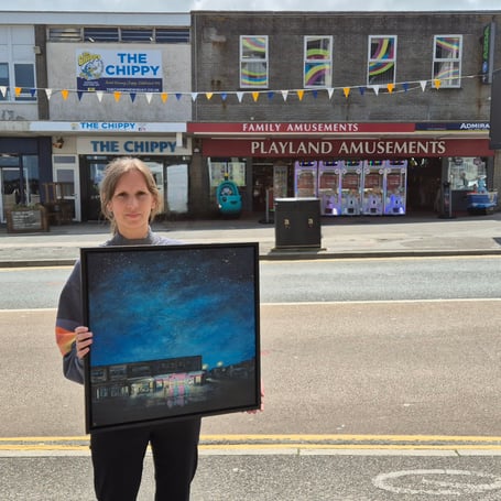 Diane Griffiths holding her Insert Coin to Begin painting in front of the Playland Amusements