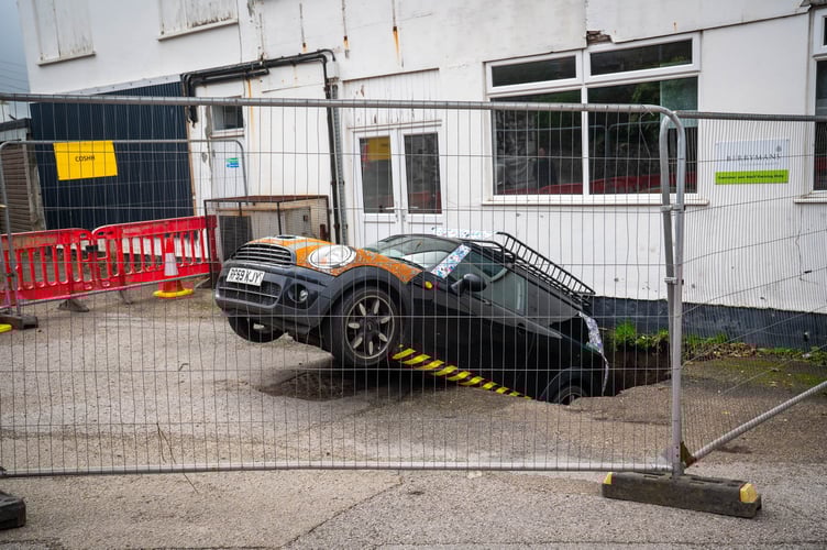 Malcolm McKenzieâ Mini Cooper, which has fallen into a sinkhole in Redruth, Cornwall.   //  A car has slipped into a sinkhole and officials are struggling to remove it - in case rescue vehicles also fall in.  The Mini Cooper became trapped in the precarious situation after a freak sinkhole opened up on Saturday afternoon outside a bakery.  Cornwall Live reports car owner Malcolm McKenzie from Redruth was told his car had fallen into a hole by a neighbour.  He went outside to find the back end of his car trapped in a hole in the ground, with the front of the Mini raised about a foot in the air.  Redruth, a mining town, has had similar incidents in the past, with authorities suspecting the hole has opened up into a disused mineshaft.  Authorities are still figuring out how to move the vehicle before it falls deeper into the mineshaft - potentially creating more collapses.  There are concerns if a recovery truck is used in the car park it could also fall in. 