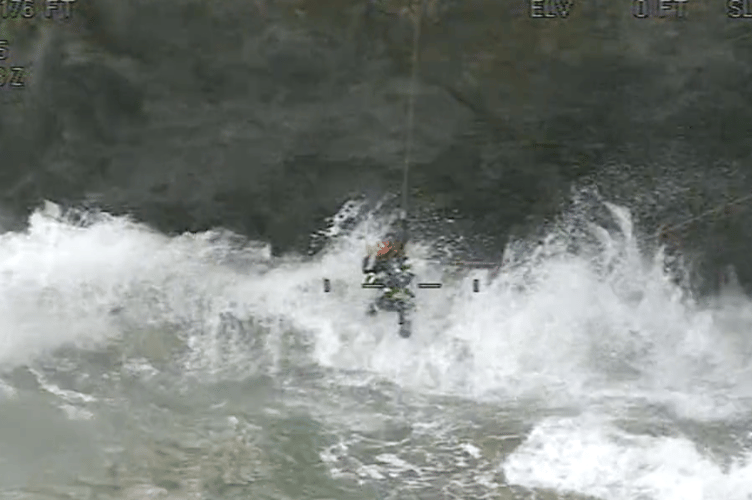 Fierce waves crashed around the rope technician and elderly man during the rescue (Picture: HM Coastguard)
