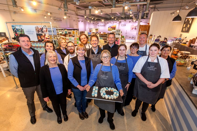 Diane Bilkey, the Great Cornish Food Store’s Café & Deli Team Leader, with a tray of cupcakes baked by her to mark the tenth anniversary. Managing director Richard Bain is pictured far left, and founder Ruth Huxley is far left on the front row. (Picture: Great Cornish Food Store)